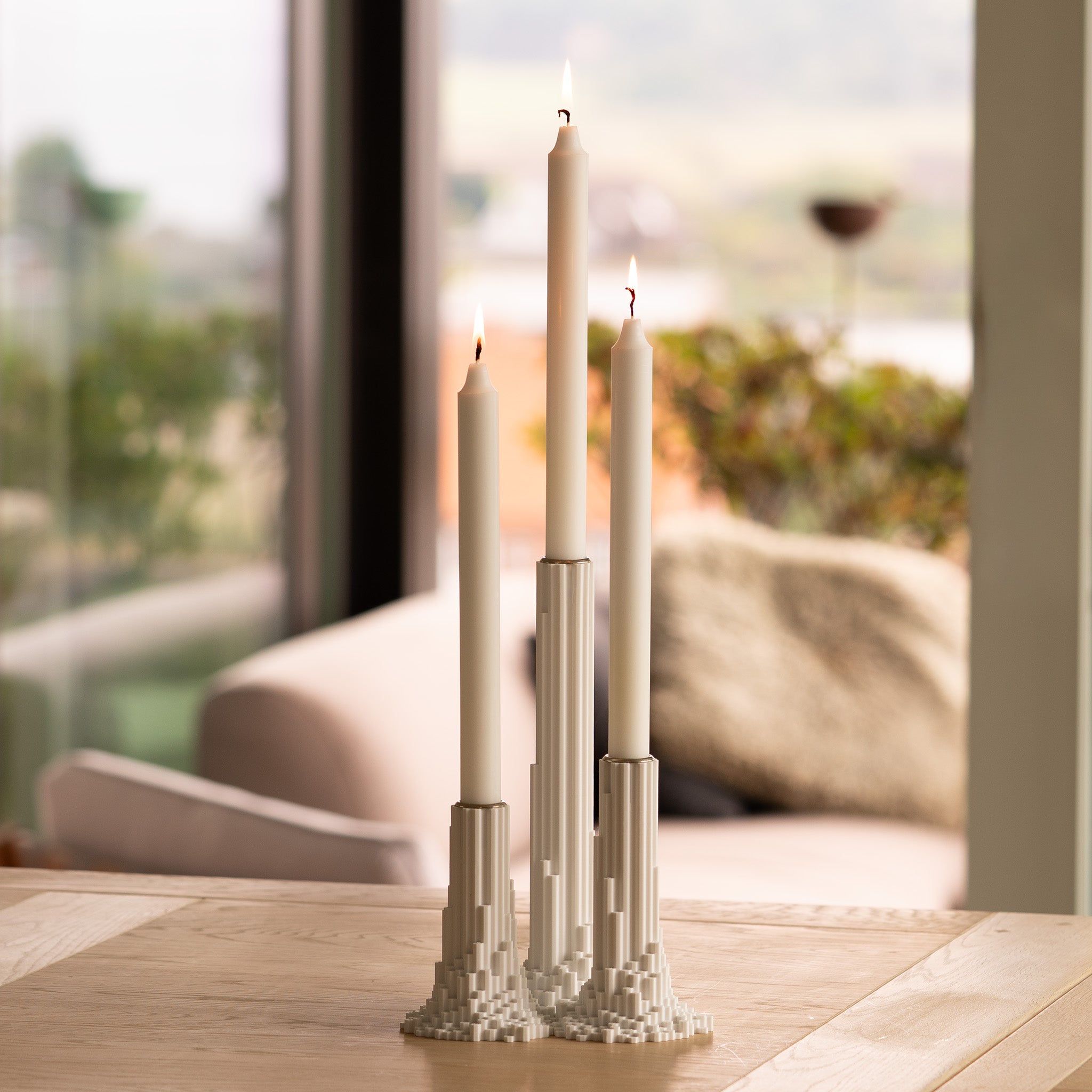 Pixelated basalt candle holders with three lit candles on a wooden table, blurred outdoor background