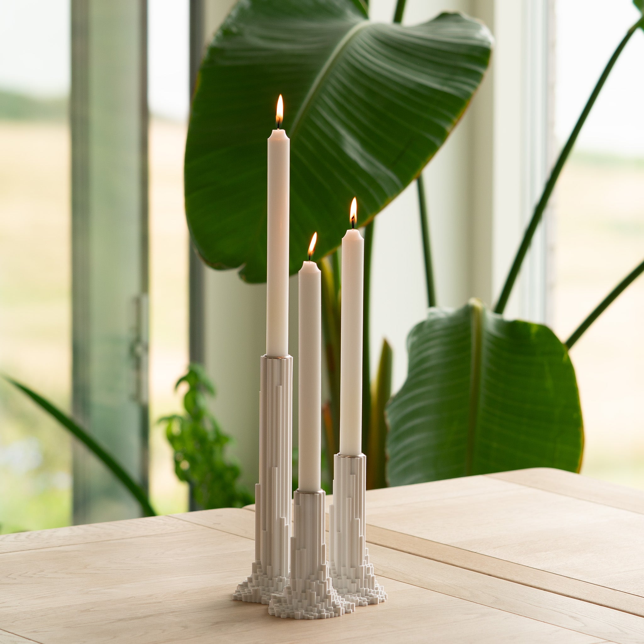 Decorative pixelated basalt candle holders with candles on a table with plants in the background