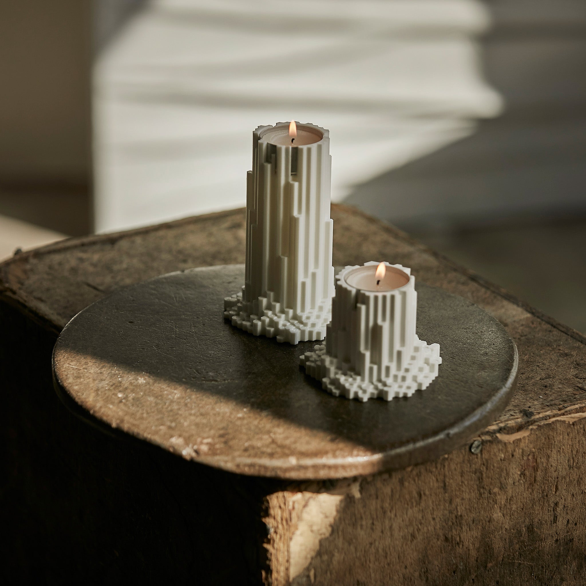 Two pixelated basalt tea light holders with lit candles on a wooden surface.