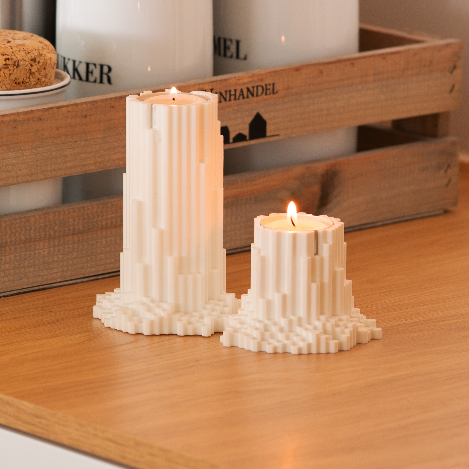 Two pixelated basalt candle holders on a wooden surface with a wooden crate in the background.