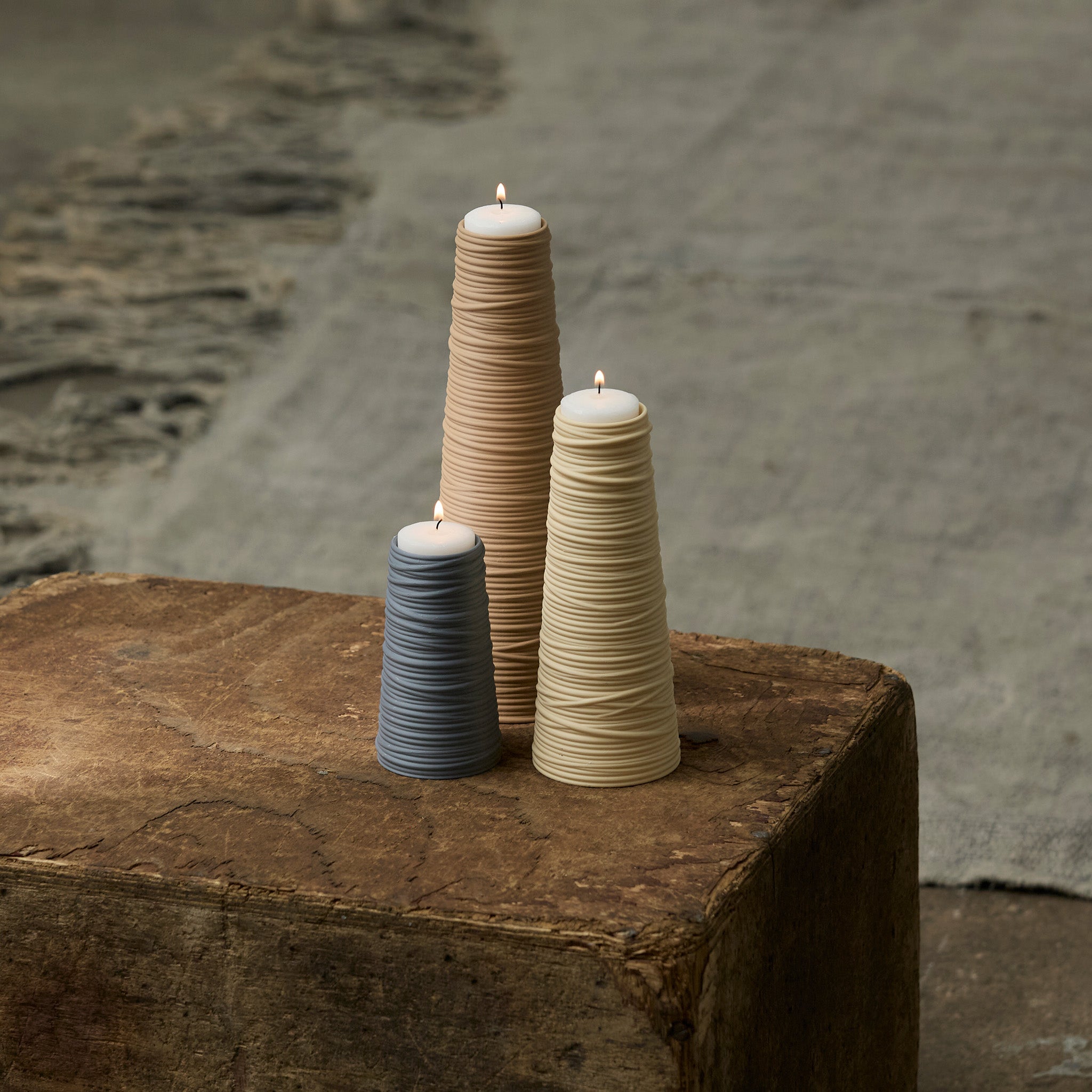 Three textured tea light holders on a stone surface with a neutral background.