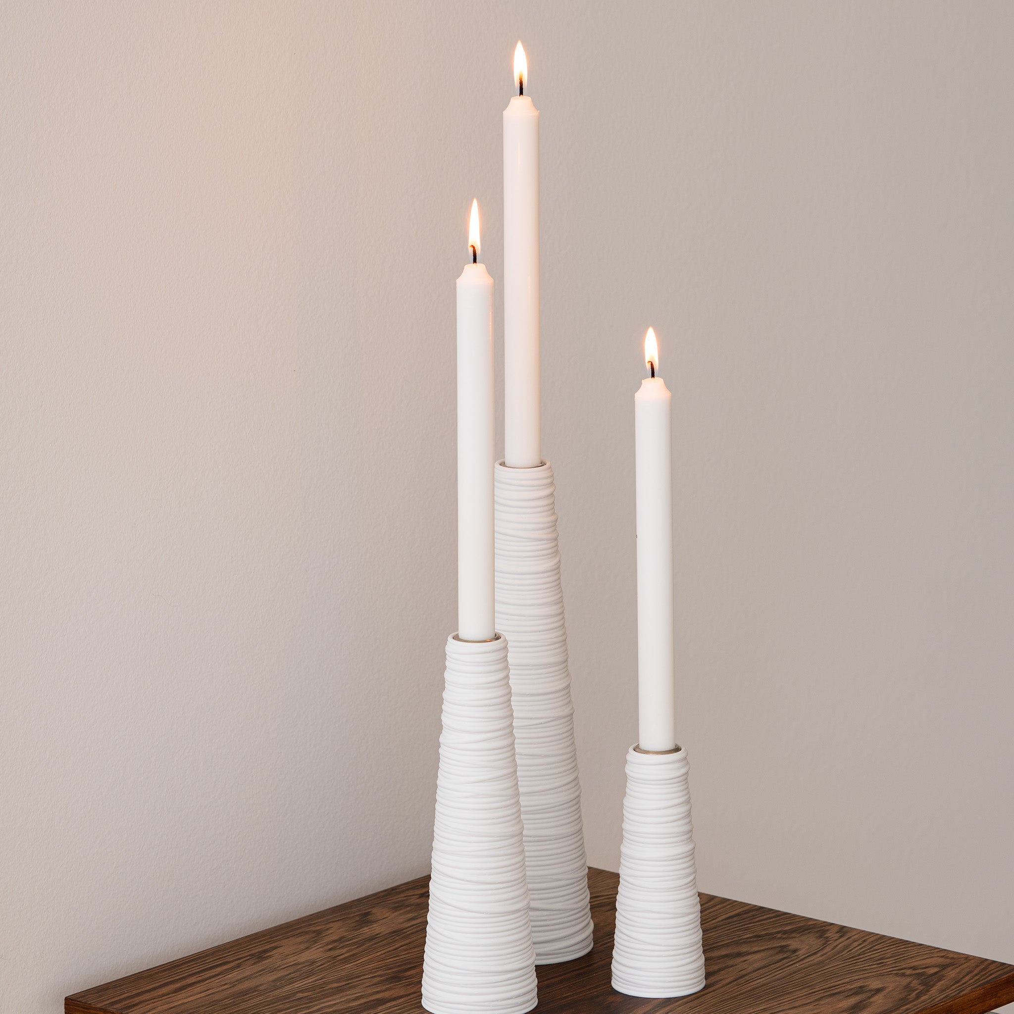 Three white candles in textured candle holders on a wooden surface with a plain background