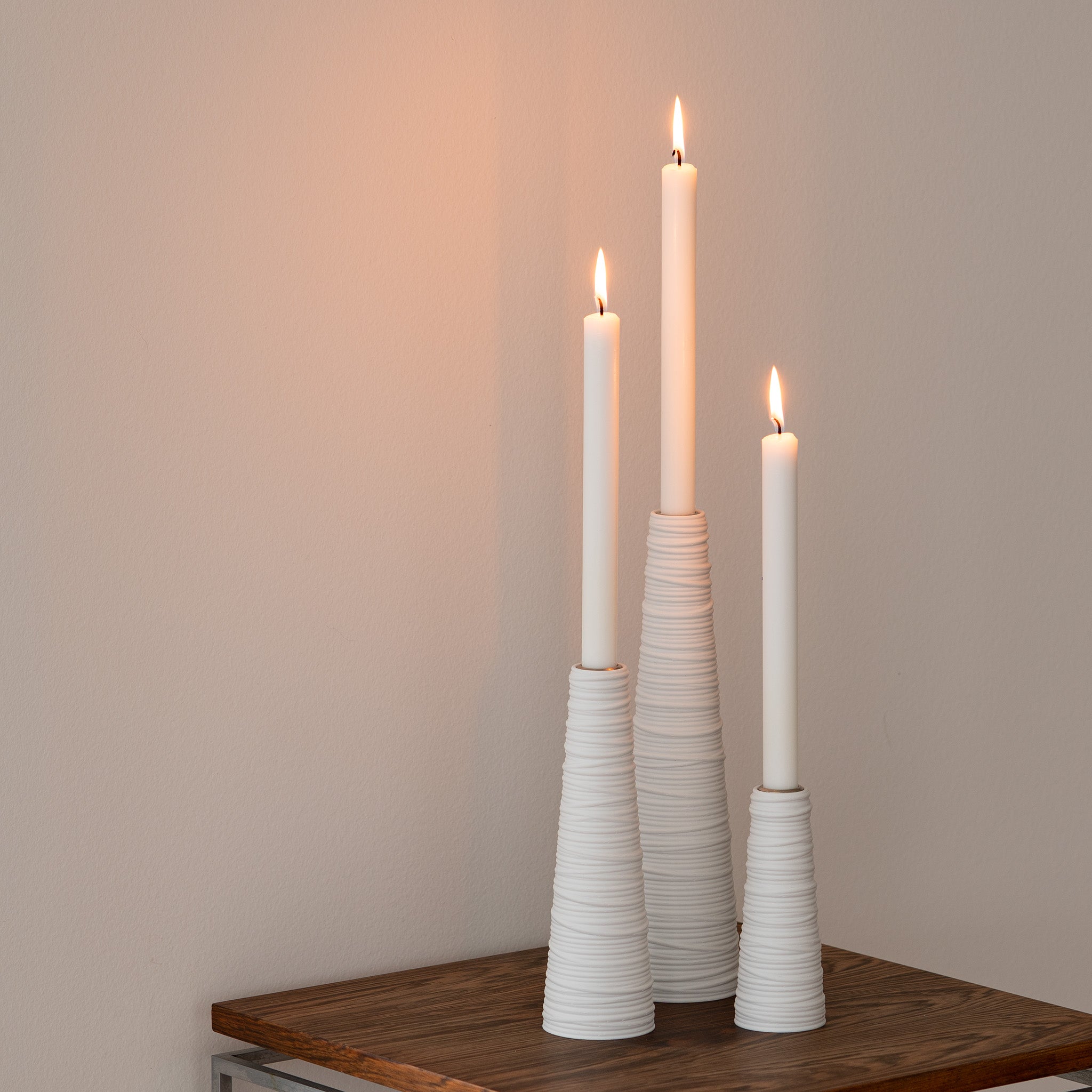 Three white candles in textured candle holders on a wooden surface with a plain background
