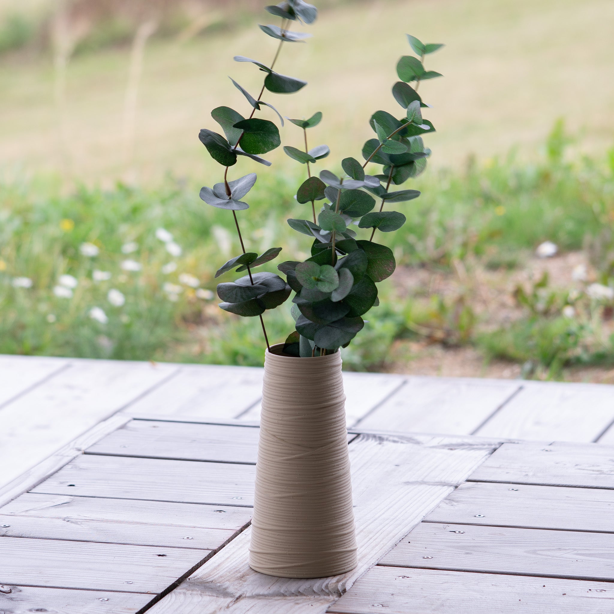 Beige textured vase with green leaves on a wooden surface outdoors