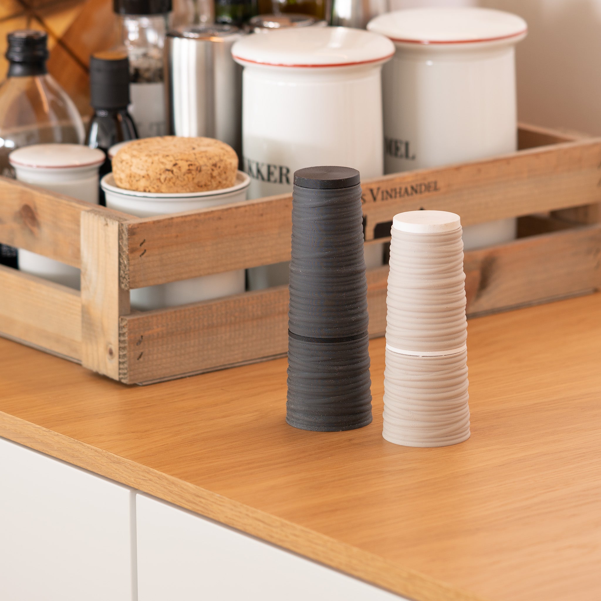 Textured salt & pepper mills on a wooden surface with a crate in the background.
