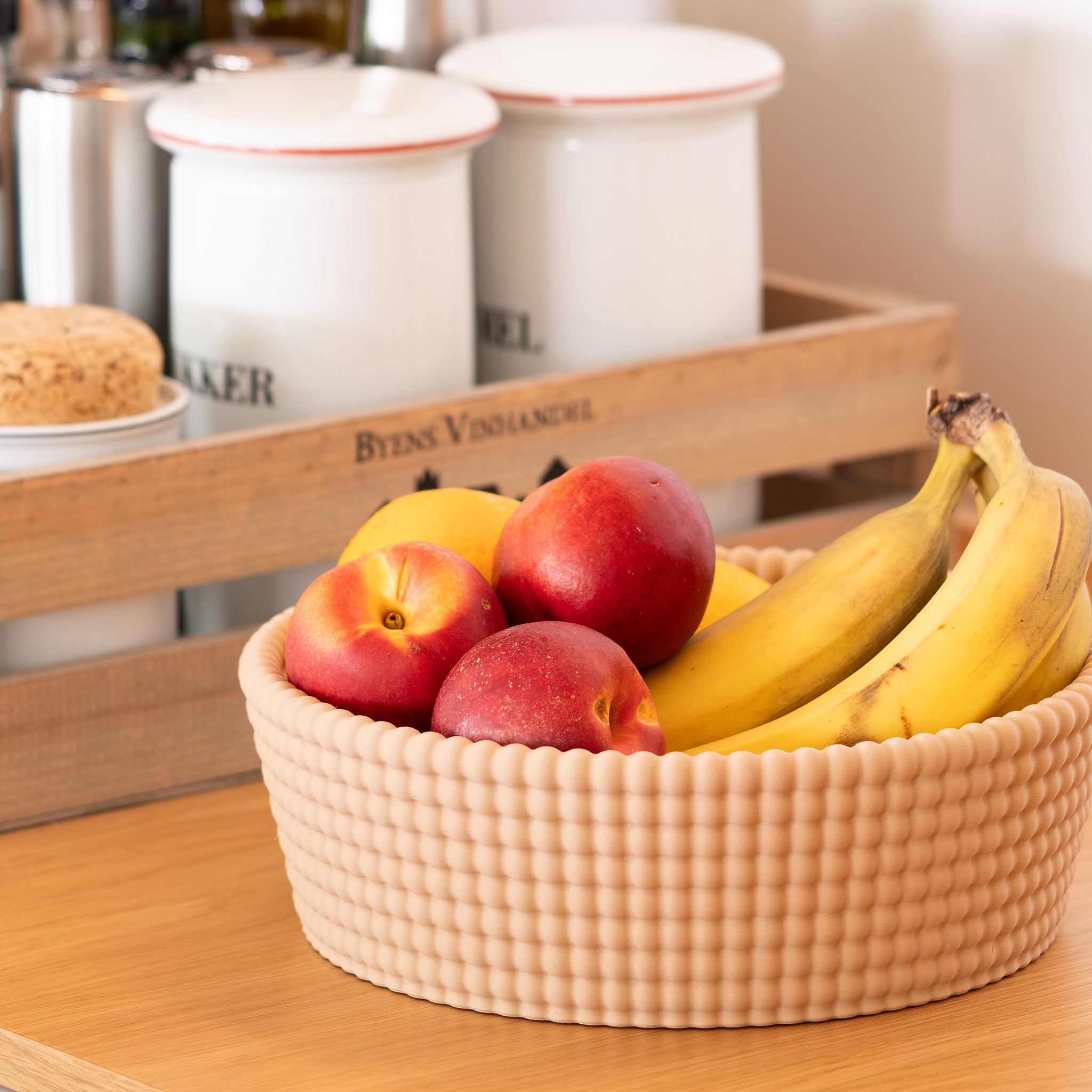 Fruit bowl with woven texture bananas and peaches on a wooden surface with kitchen background