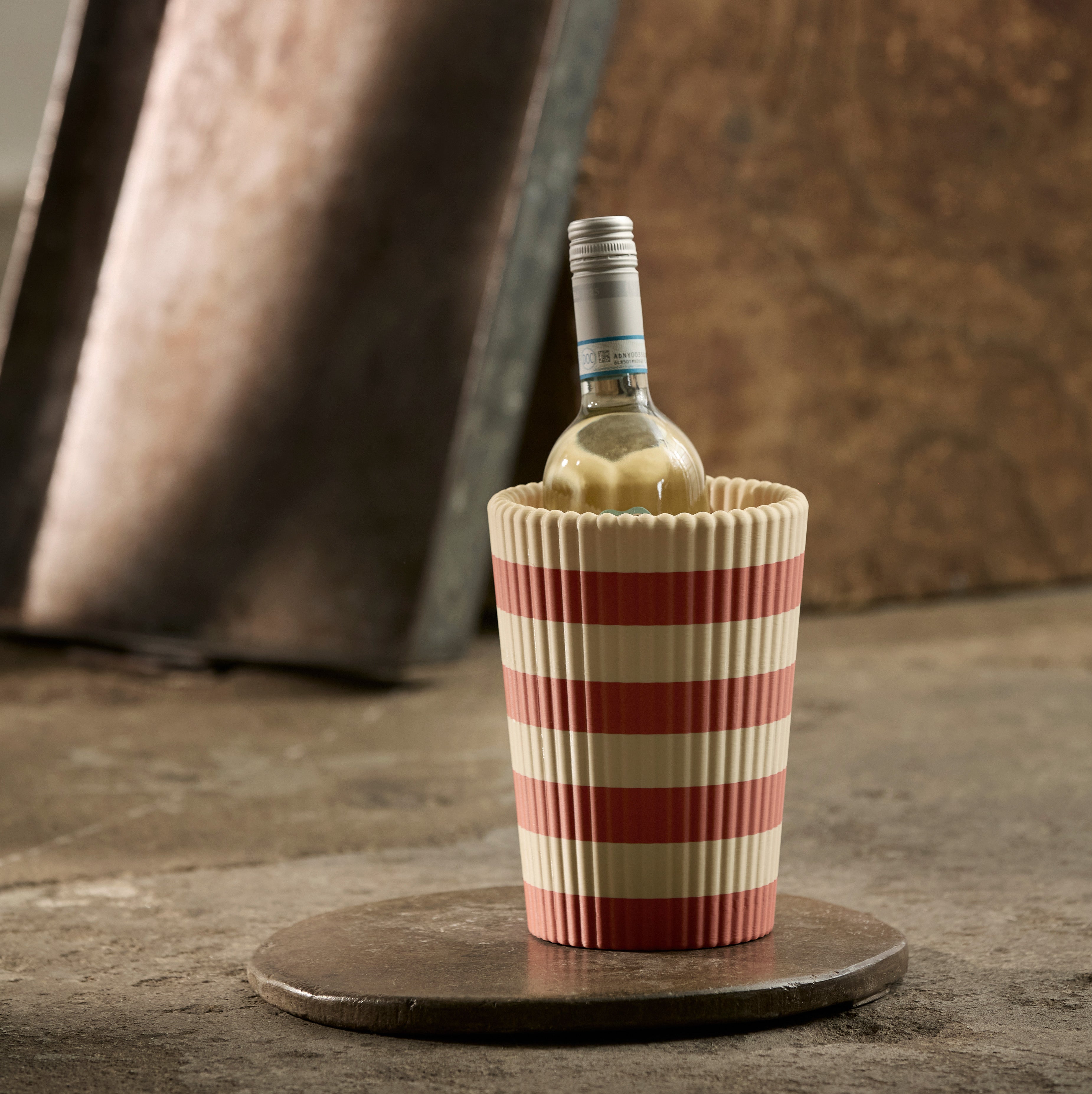 Wine bottle in a red and beige striped wine cooler on a rustic surface